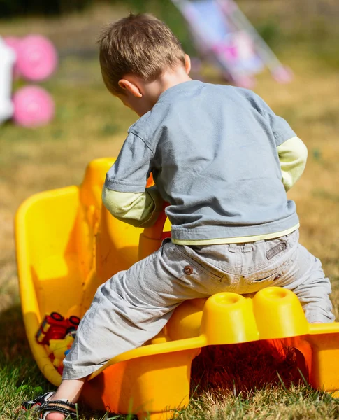 Petit garçon tout-petit jouant sur une voiture jouet jaune — Photo