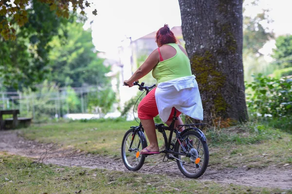 Obézní žena na koni na kole v parku — Stock fotografie