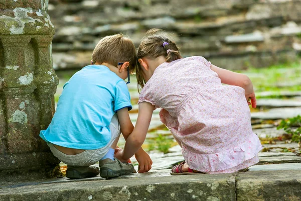 在一块长满苔藓的石头旁边的地面上玩的两个孩子 — 图库照片
