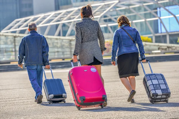 Três pessoas puxando sua bagagem para a entrada do aeroporto — Fotografia de Stock