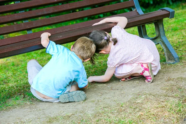 Two cute kids looking for something under the bench in the park Royalty Free Stock Photos