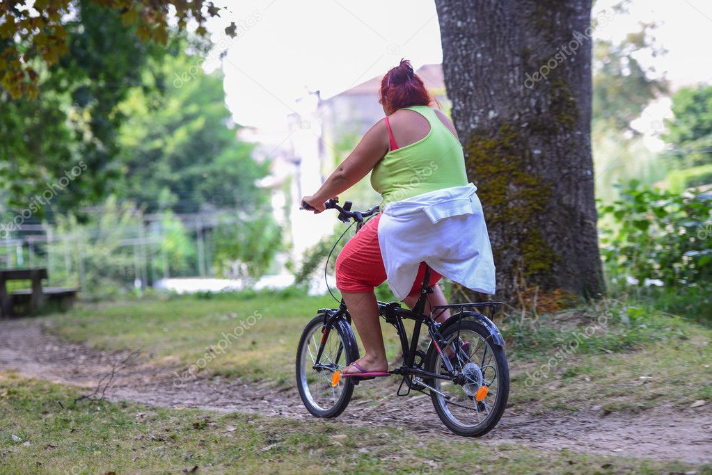Overweight woman riding on a bicycle in a park