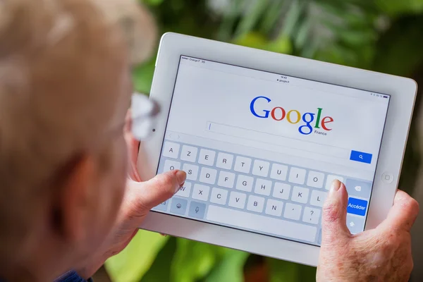 París, Francia - 27 de abril de 2015: Mujer mayor usando tableta con la página de inicio de búsqueda de Google en una pantalla de ipad — Foto de Stock