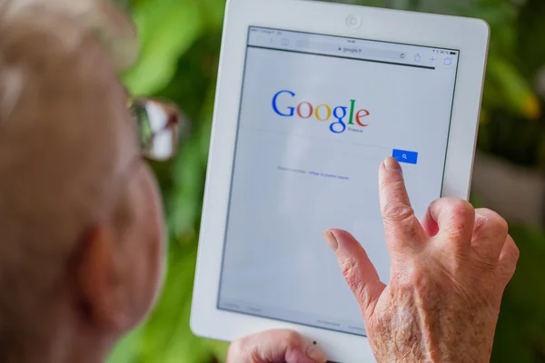 Paris, France - April 27, 2015: Senior woman using tablet with Google search home page on a ipad screen — Stock Photo, Image