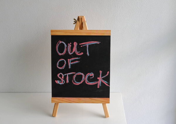 Close-up handwritten words out of stock on chalkboard standing on white wooden table against white concrete wall 