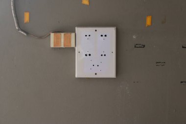 Kapalı bir dükkanın duvarına monte edilmiş terk edilmiş bir yük merkezi. Beyaz kutunun tüm dahili devreleri boş, sadece montaj delikleri görünüyor. Solda, yapışkan bantlarla maskelenmiş bir elektrik prizi var..