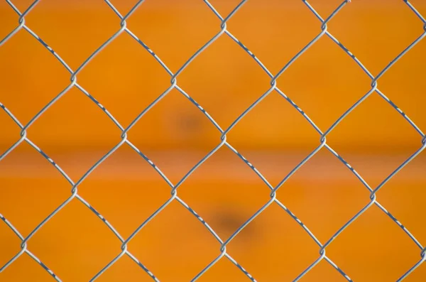 Metal mesh fence against orange background. Close-up of gray seamless mesh.