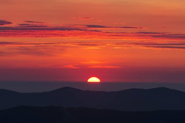 Dağlarda gün doğumu. Kan kırmızısı gökyüzü birkaç bulutla kaplıdır. Dağların siluetleri görünür..
