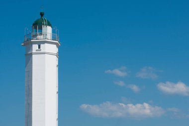 Mavi gökyüzünün arka planında beyaz deniz feneri. Beyaz bulutlar gökyüzünde süzülür.