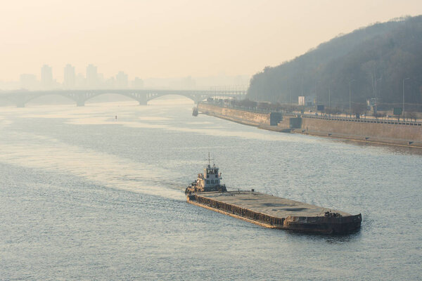 River transport. Barge and tugboat are on the river against the background of the bridge and urban views in the morning haze.