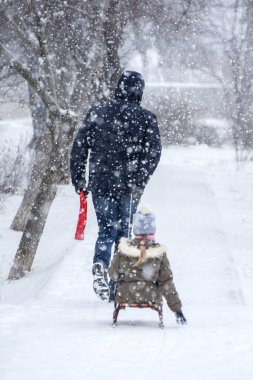 Baba kızını bir kızağa bindiriyor. Yumuşak kar yağıyor. Kış aktiviteleri ve tatiller. Seçici odak.