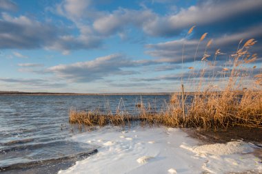 Güzel nehir manzarası. Suda küçük dalgalar ve kıyıya yakın beyaz köpükler. Kasvetli hava ve fırtına bulutları. Nehirde balık tutmak.