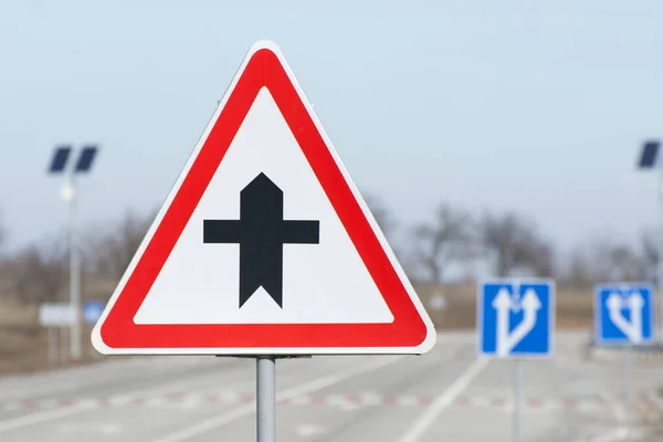 Road sign warning of a crossroads. Regulation of traffic on a highway. Empty roadway with directional signs.