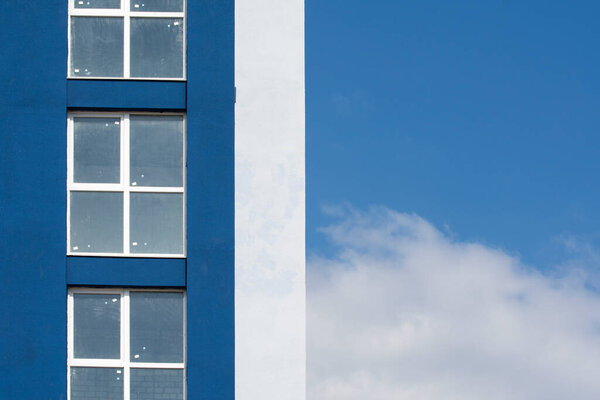 Facade of an unfinished apartment building. The wall of the apartment and the blue sky divide the frame in half.