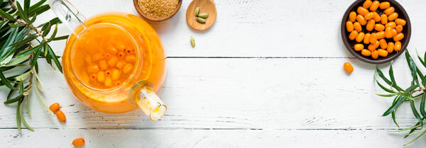 Чай с облепихой ягод в стеклянном чайнике на белом деревянном фоне, баннер. Сезонный осенний острый чай с облепихой.