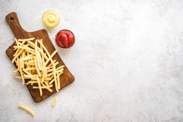 French fries on board with ketchup and cheese sauce, top view, copy space. Homemade french fries on white background.