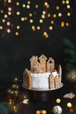 Köy evleri şeklinde zencefilli kurabiyelerle süslenmiş Noel pastası. Kış tatili için Noel süslü ve çelenkli şenlikli pasta.