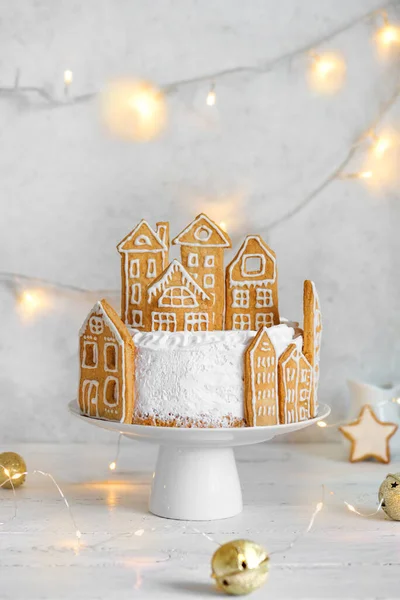 Christmas cake decorated with gingerbread cookies in shape of village houses, copy space. White Festive Cake with Christmas decor and garlands for winter holidays.
