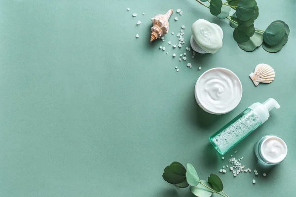 Sea mineral cosmetic products. Skin care, body treatment products, eucalyptus leaves, sea salt and shells  on green background, top view, copy space. Spa and natural skin care concept.