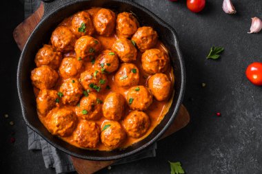 Domates soslu ev yapımı köfteler. Biftek köfteleri siyah arka planda dökme demir tavada.