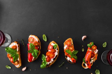 Domatesli, krem peynirli, kırmızı biberli ve fesleğenli sandviçler koyu arka planda, üst manzara, fotokopi alanı. Şarap için geleneksel İtalyan aperatifi. Izgara bruschetta tostu..