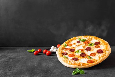 Mozarella, domates ve salamlı geleneksel İtalyan pizzası. Fırından yeni çıkmış sıcak pizza, siyah arka plan, fotokopi alanı. Pizza teslimatı ya da pizza tanıtım konsepti.