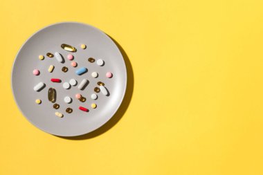 Birçok vitamin hapı ve takviyeler gri tabakta yemek olarak, sarı arka planda. Besin takviyesi konsepti. İlaç alıyorum. Yemek yerine hap..