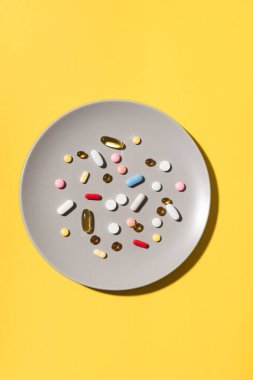 Birçok vitamin hapı ve takviyeler gri tabakta yemek olarak, sarı arka planda. Besin takviyesi konsepti. İlaç alıyorum. Yemek yerine hap..
