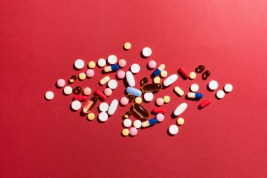 Çok renkli tabletler, haplar, kırmızı arka planda kapsüller, kopyalama alanı. Çeşitli ilaç tabletleri ve haplar, vitamin ve besin takviyeleri konsepti..