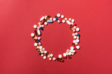 Çok renkli tabletler, haplar, kırmızı arka planda kapsüller, yuvarlak çerçeve, kopyalama alanı. Çeşitli ilaç tabletleri ve haplar, vitamin ve besin takviyeleri konsepti..