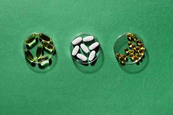 Vitamins capsules on green background, top view, copy space. Food supplements: fish oil, omega 3, omega 6, omega 9, vitamin A, D3,  E, B, calcium.