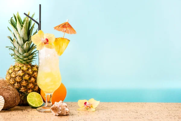 Summer tropical cocktail drink, fruits and flowers, blue sea background, copy space. Summer vacation and beach relax concept. Golden Eye pineapple and rum cocktail recipe.