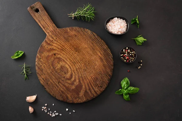 Boş ahşap tahta tahta, siyah mutfak masasında bitkiler ve baharatlar, üst manzara, düz yatak. Tahta pizza tabağı, kopyalama alanı. Gıda arkaplanı.