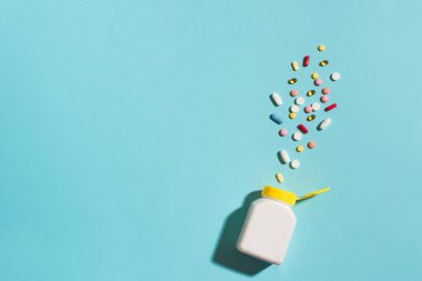 Çok renkli tabletler, haplar, plastik kapsüller mavi arka planda, kopyalama alanı. Çeşitli ilaç tabletleri ve haplar, vitamin ve besin takviyeleri konsepti..