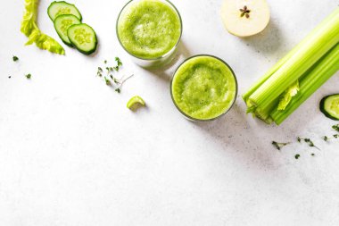 Yeşil sebze suyu ya da bardakta meyve suyu. Taze sıkılmış detoks yeşil meyve suyu ve bir demet organik kereviz, salatalık, beyaz masada elma, üst manzara, kopyalama alanı.