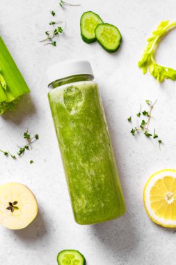 Plastik şişede yeşil meyve püresi ve beyazın üzerindeki malzemeler, üst manzara. Taze çiğ detoks smoothie veya sağlıklı yemek için yeşil meyve suyu..