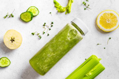 Plastik şişede yeşil meyve püresi ve beyazın üzerindeki malzemeler, üst manzara. Taze çiğ detoks smoothie veya sağlıklı yemek için yeşil meyve suyu..