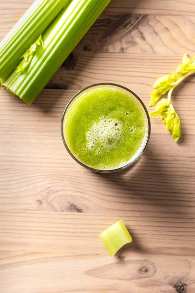 Celery juice in glasses. Fresh squeezed detox green juice and bunch of organic celery on wooden table, top view, copy space.