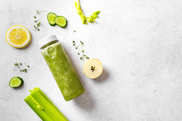Green smoothie in plastic bottle and ingredients on white, top view, copy space. Fresh raw detox smoothie or green juice for healthy eating.