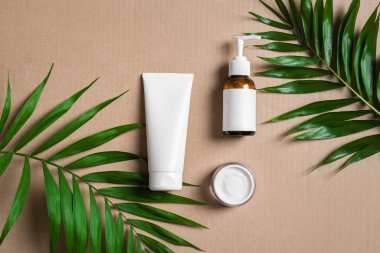 Doğal kozmetik krem, vücut losyonu ve bej arka planda yeşil bitkiler, üst manzara. Dermatoloji, organik cilt bakımı ve yeşil palmiye yapraklı spa konsepti.