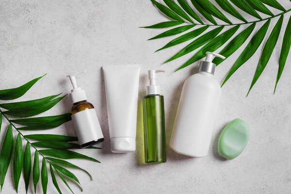 Natural cosmetic products and green plants on gray stone background, top view. Dermatology, organic skin care and spa concept with green palm leaves.