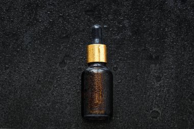 Damlatan güzellik ürünü (yüz serumu, sıvı, emülsiyon, temel yağ) ıslak siyah taş zemin üzerinde su damlaları ile birlikte. Doğal cilt bakımı nemlendirici, kozmetoloji konsepti.