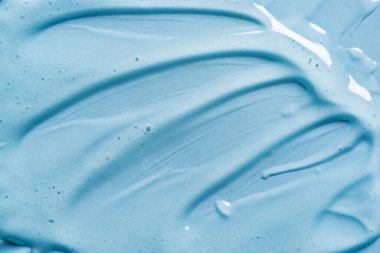 Mavi arkaplanda jel dokusu var. Yakın plan. Şeffaf jel kozmetik ürününün vuruşları.