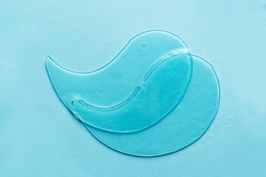 Hydrogel blue eye patches on blue background close up. Cosmetic moisturizing under eye patches with collagen.