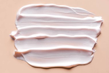 Facial highlighter cream swatch on nude background close up. Light facial cream sample strokes.