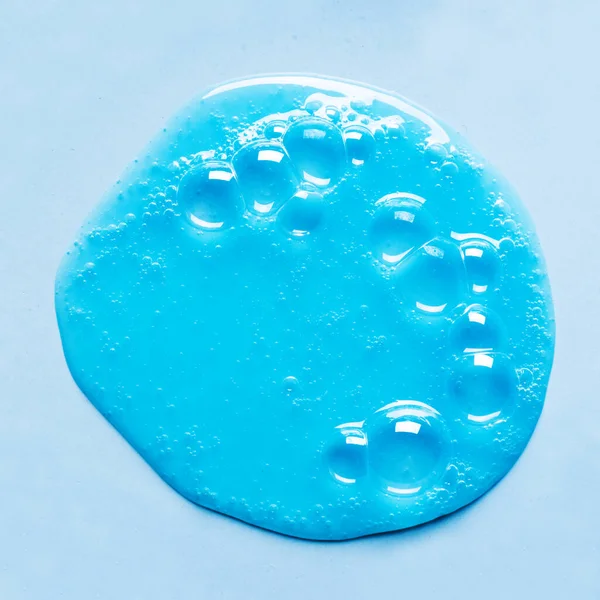 蓝色洗发水或淋浴液样品在蓝色背景上的水坑 带有气泡的蓝色凝胶化妆品 — 图库照片