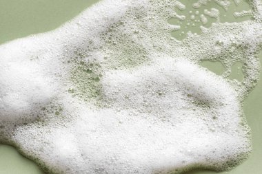 Yüz temizleyici köpük örneği. Yeşil arka planda beyaz köpük köpüğü. Sabun, duş jeli, şampuan köpüğü dokusu yakından..
