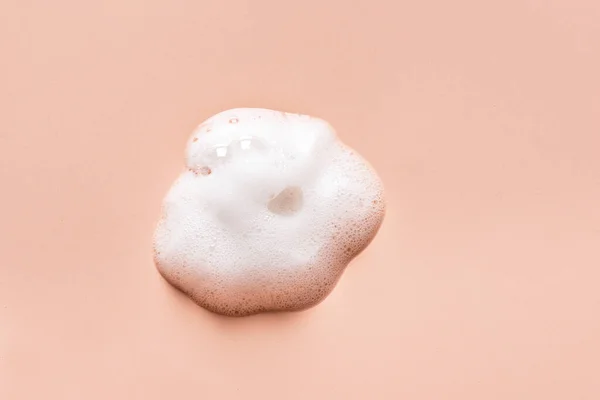 Face cleansing mousse sample. White cleanser foam bubbles on nude background. Soap, shower gel, shampoo foam texture closeup.