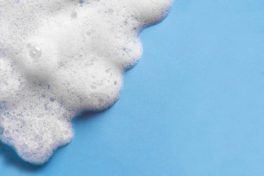Yüz temizleyici köpük örneği. Mavi arka planda beyaz köpük temizleyici köpükler, kopyalama alanı. Sabun, duş jeli, şampuan köpüğü dokusu yakından..