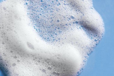 Yüz temizleyici köpük örneği. Mavi arka planda beyaz köpük köpüğü. Sabun, duş jeli, şampuan köpüğü dokusu yakından..